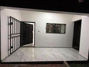 Una habitación con suelo de baldosas, una puerta con reja de metal y una ventana con barrotes, además de una pared blanca.