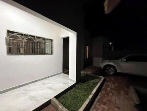 Un edificio moderno con fachada blanca, una ventana con barrotes, un acceso pavimentado y un coche estacionado cerca.