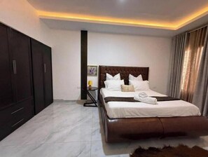 Un dormitorio con una cama grande, un armario oscuro y una mesita de noche con lámpara.