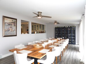 A dining area with a long wooden table, white chairs, and a ceiling fan. - Beach Lodge w/ Hot Tub & Sauna (Port Rowan)