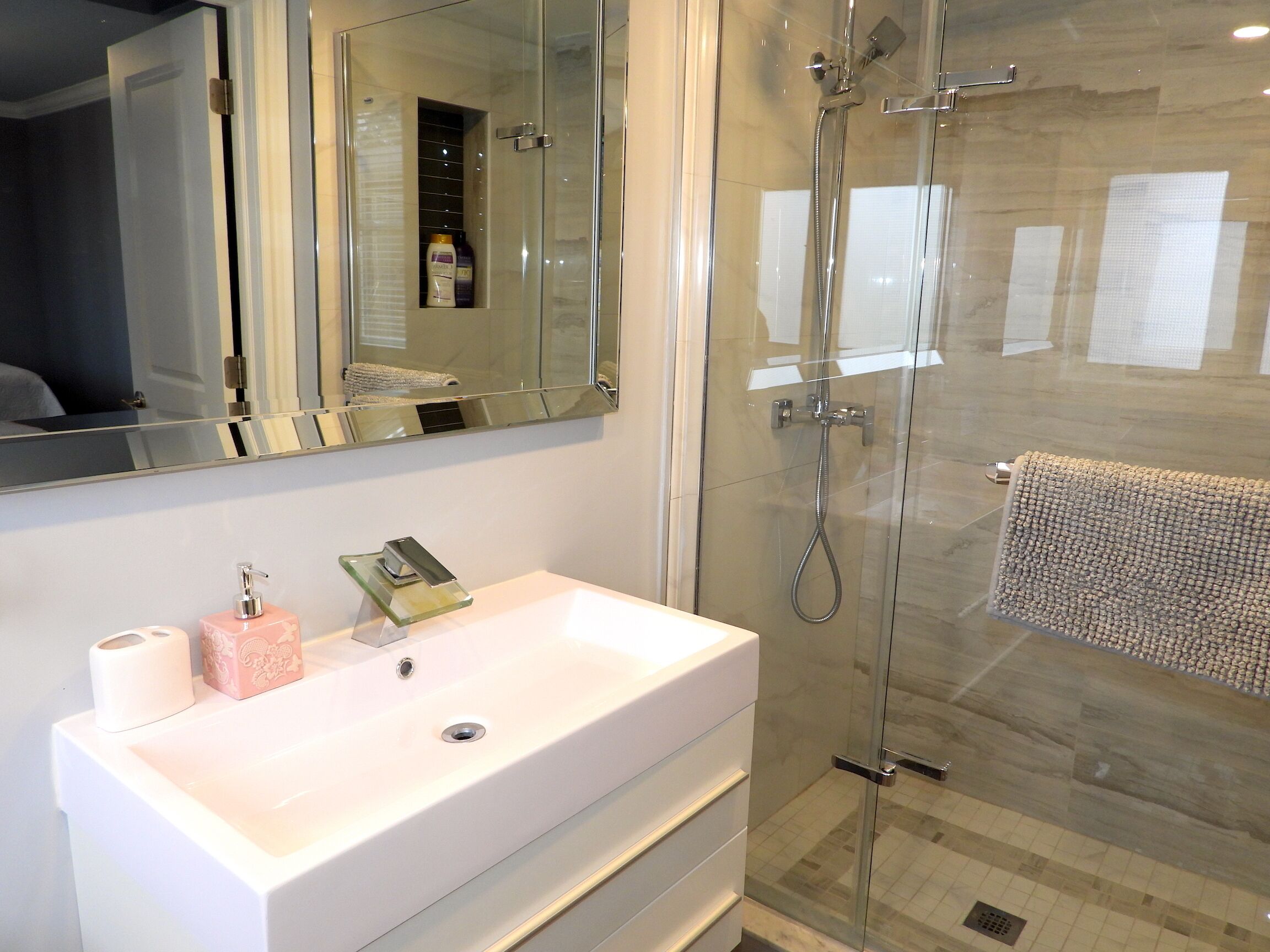 Un baño moderno con un lavamanos blanco, cabina de ducha de vidrio y un espejo grande.