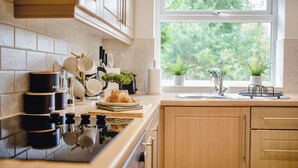 Una cocina con ventana, armarios, estufa y diversos utensilios.
