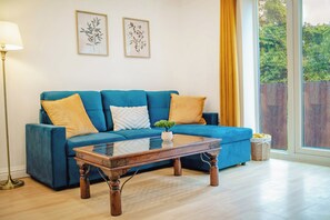 A blue sofa with cushions, a wooden coffee table, a floor lamp, and two framed botanical prints on the wall. - Cosy Central Apartment | Free Parking | 6PPL (Sheffield)