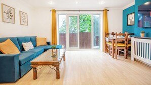 Una sala de estar con un sofá azul, una mesa de centro de madera y un comedor con sillas y una mesa de madera.