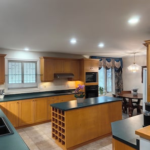 A kitchen with wooden cabinets, a central island, a dining area with a table and chairs, and a window with decorative curtains.