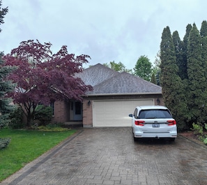 A residential house with a garage, a driveway, and a parked white car. - L&V | Hearthwood Retreat | 4 Kings | Pool Table & Deck | Gather & Unwind (Niagara-on-the-Lake)