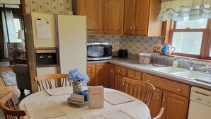 Una cocina con armarios de madera, un refrigerador, un microondas y una mesa de comedor con sillas.
