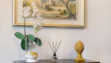 A vase with an orchid, a small glass container with reed sticks, and a decorative urn on a wooden table against a wall with a framed painting.