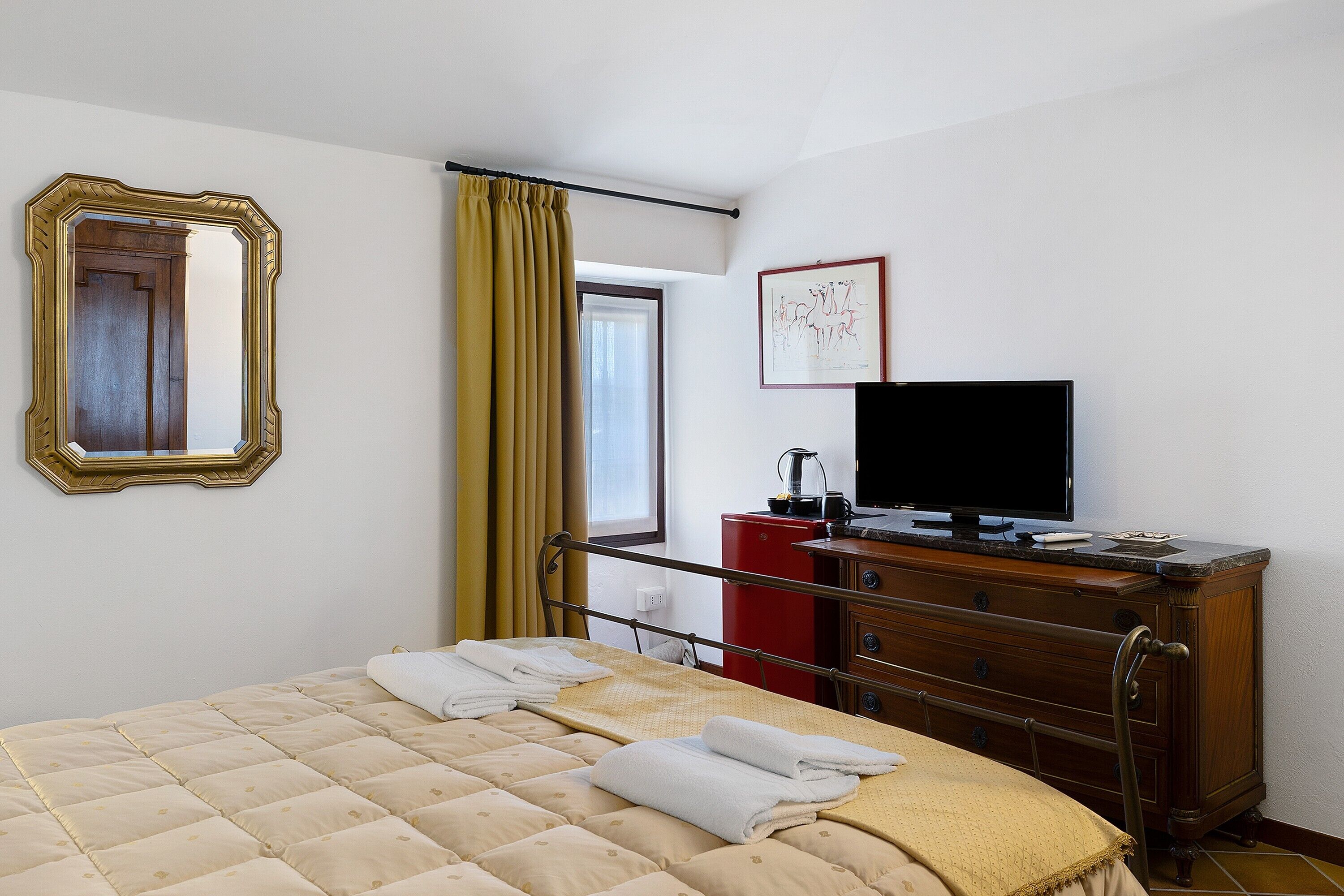 Une chambre d’hôtel avec un lit, une télévision, une commode, un miroir et une fenêtre avec des rideaux.