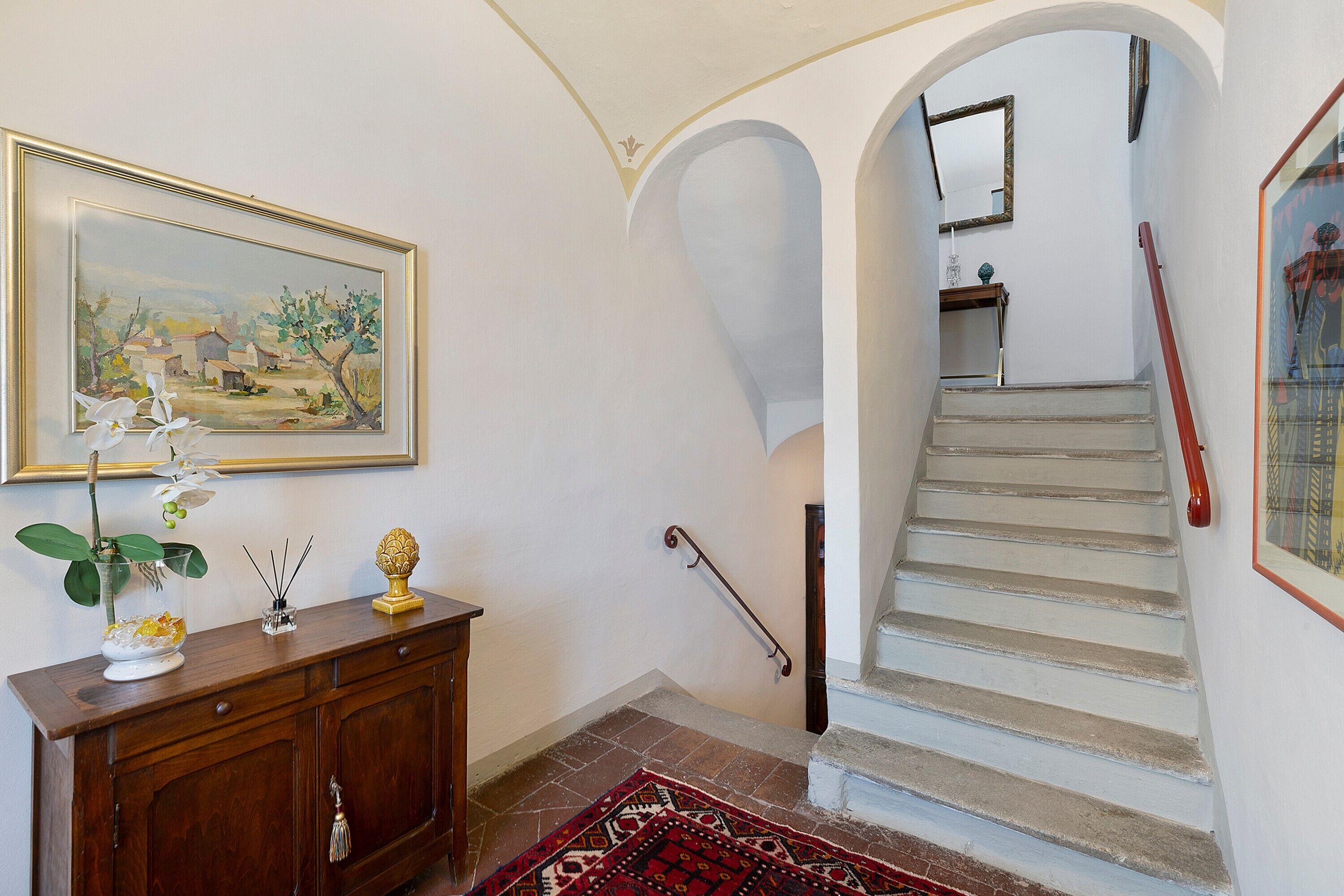A staircase with a handrail, a framed painting on the wall, and a wooden cabinet with decorative items.