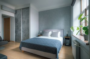 A modern bedroom with a bed, bedside tables, a radiator, and a window with a plant. - Stylish apartment with AC in the heart of Riga Centre (Riga)