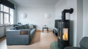 A modern living room with a sofa, a small table with a vase, a fireplace, and a large window. - Stylish apartment with AC in the heart of Riga Centre (Riga)