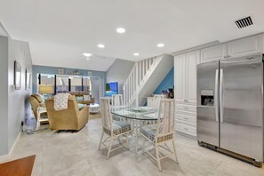 A modern kitchen with a stainless steel refrigerator, white cabinetry, and a glass dining table with white chairs. - Ocean Village 2 bd 2 bath w loft, walk to beach, pools, golf. Fully furnished. (Fort Pierce)