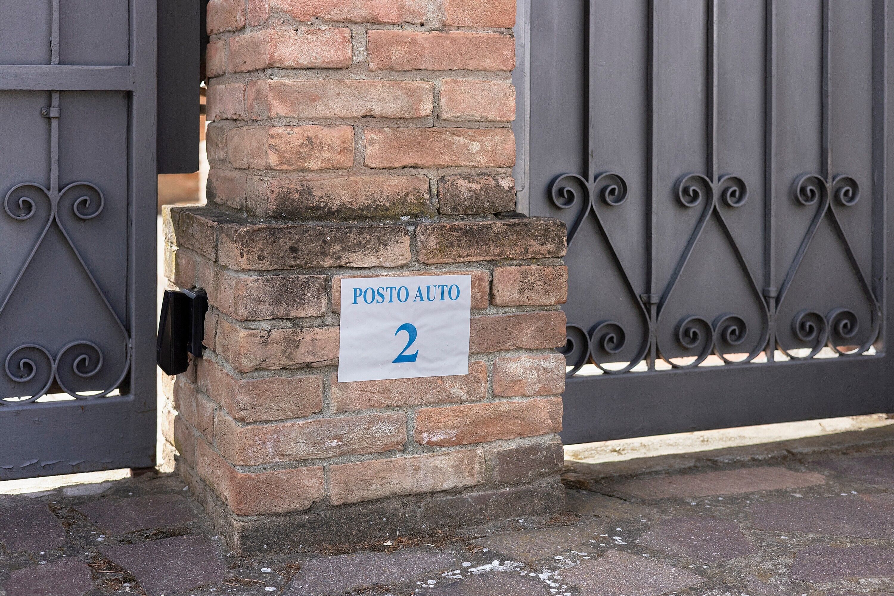 A brick pillar with a sign reading 'POSTO AUTO 2' and a metal gate.