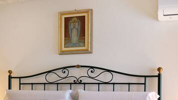 A bed with a metal headboard, white bedding, and a framed picture on the wall.