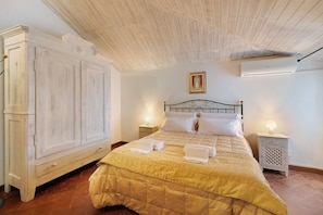 A bedroom with a bed, two bedside tables with lamps, a wardrobe, and an air conditioning unit.