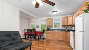 A compact kitchen with wooden cabinets, a dining area with a red tablecloth, and a black sofa. - Lem's Paradise #1 | 300+ ft Lake Huron Shoreline & Mackinac Views (Cheboygan)