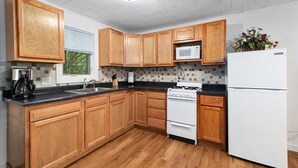 A kitchen with wooden cabinets, a microwave, a stove, and a refrigerator. - Lem's Paradise #1 | 300+ ft Lake Huron Shoreline & Mackinac Views (Cheboygan)