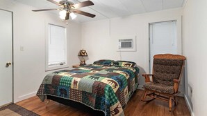 A bedroom with a bed, a chair, a ceiling fan, and two windows with blinds. - Lem's Paradise #1 | 300+ ft Lake Huron Shoreline & Mackinac Views (Cheboygan)