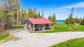 A small cabin with a red roof, a porch, and a view of a lake.