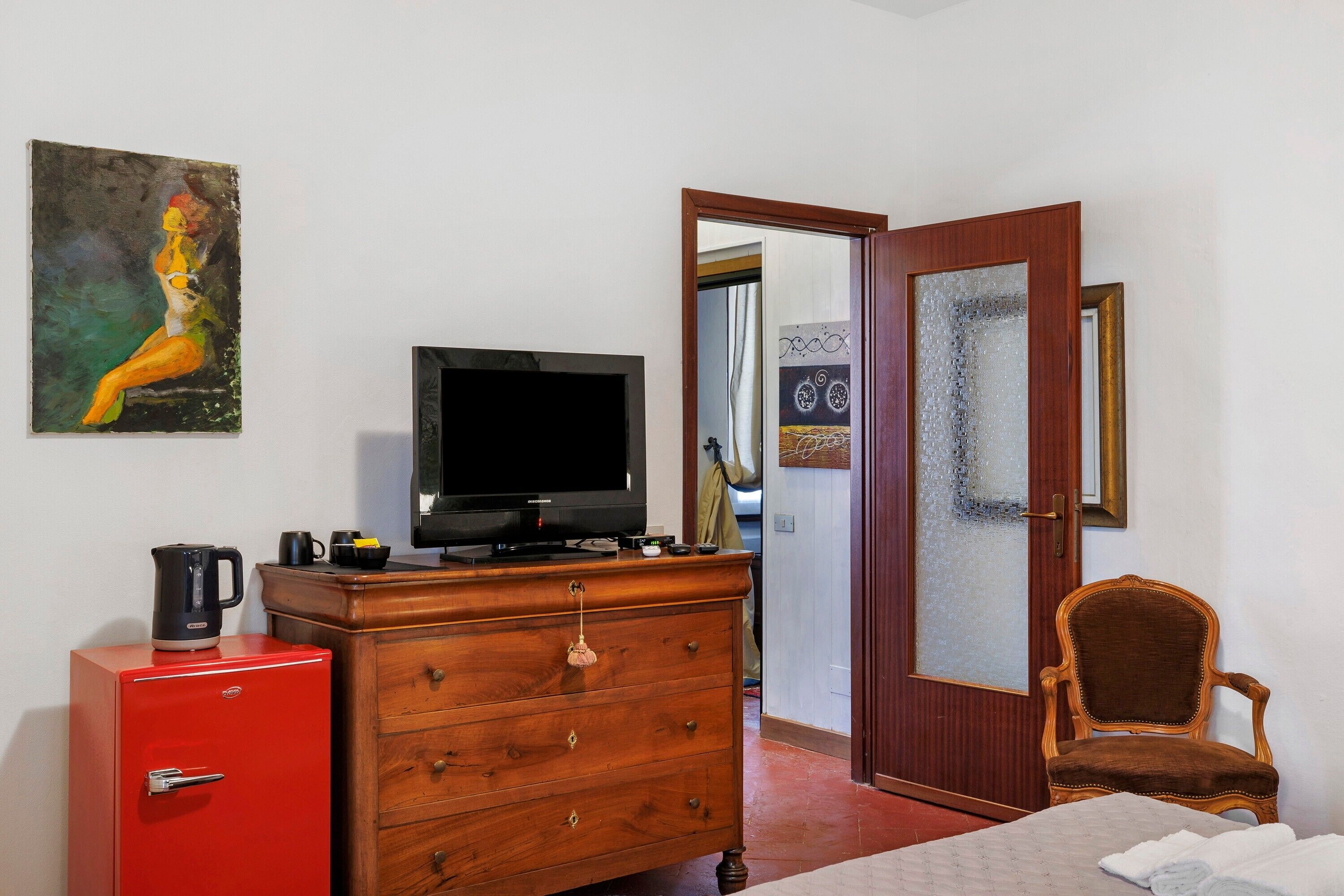 A room with a television, a red filing cabinet, a wooden dresser, a brown chair, and a painting on the wall.
