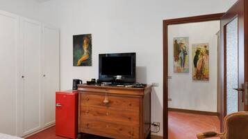 Una habitación con un televisor sobre un aparador de madera, un refrigerador rojo y dos cuadros en la pared.