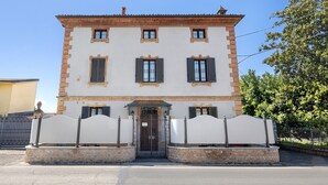 Un edificio a due piani con facciata simmetrica, un ingresso centrale con porta e finestre, e un vialetto recintato.
