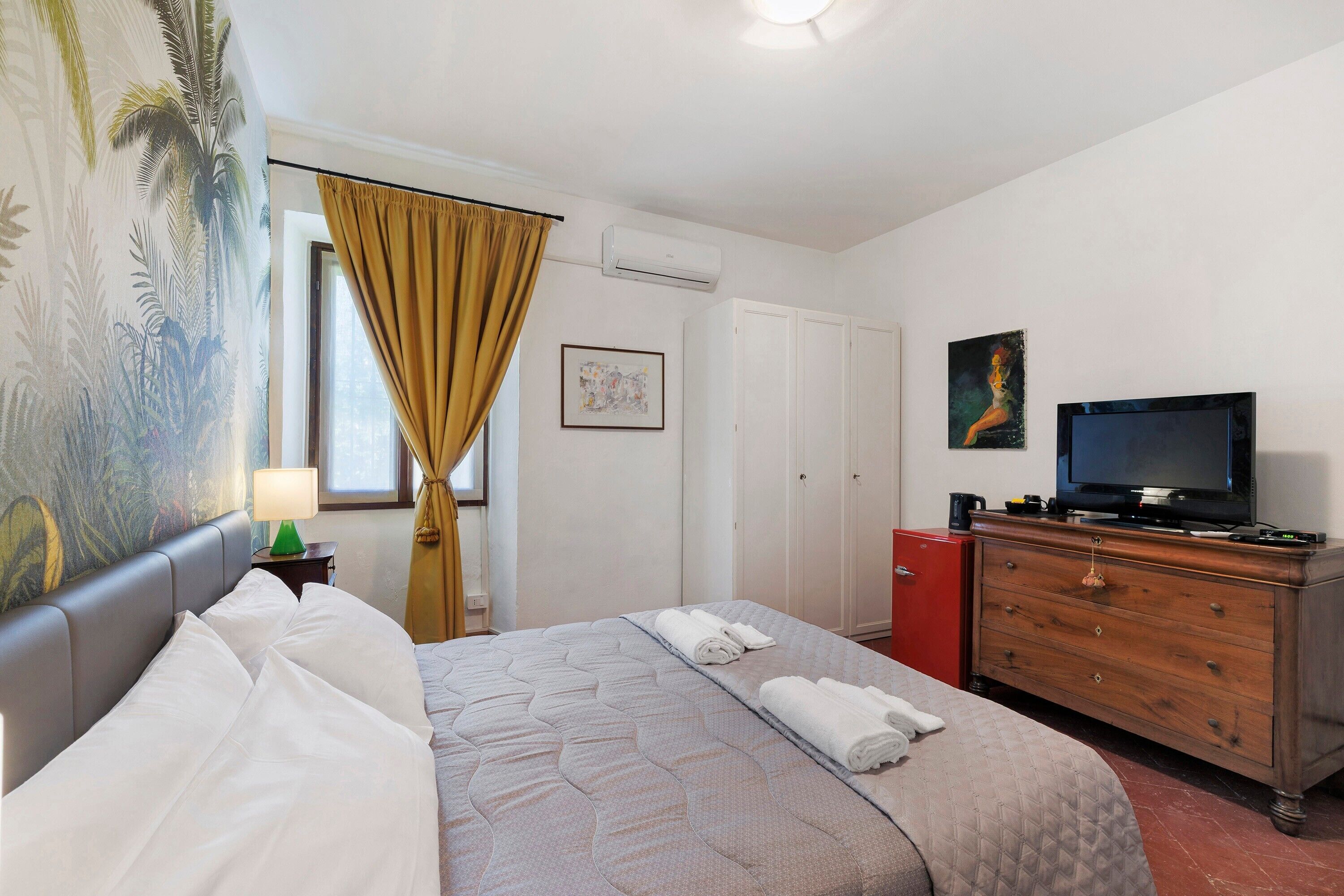 Une chambre d’hôtel avec un lit, une télévision, une commode, un placard rouge et un tableau accroché au mur.