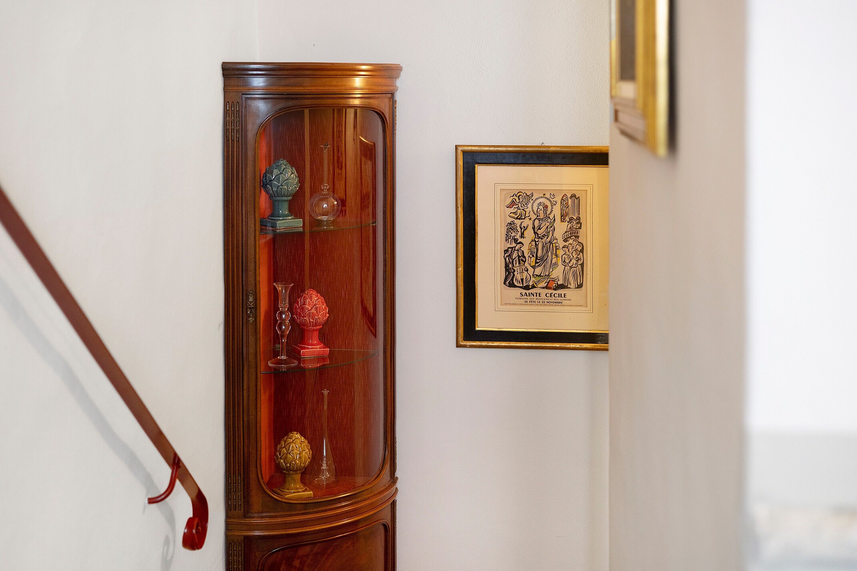 Ein Holzschrank mit Glastüren, ein gerahmtes Zertifikat und ein Stock mit rotem Griff, der an der Wand lehnt.