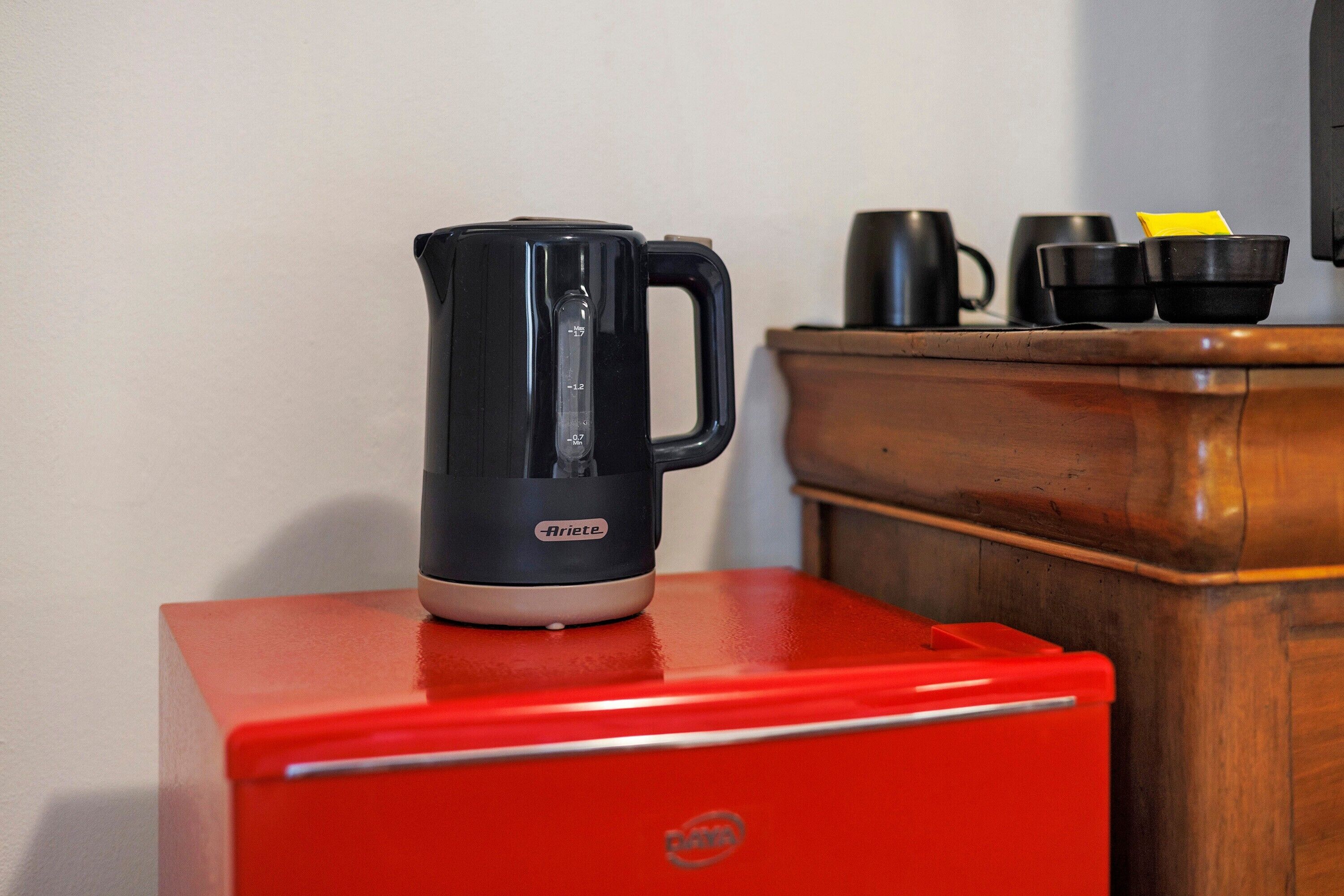 Una cafetera negra sobre un electrodoméstico rojo, un armario de madera y tazas negras.