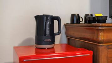 Una cafetera negra sobre un electrodoméstico rojo, un armario de madera y tazas negras.