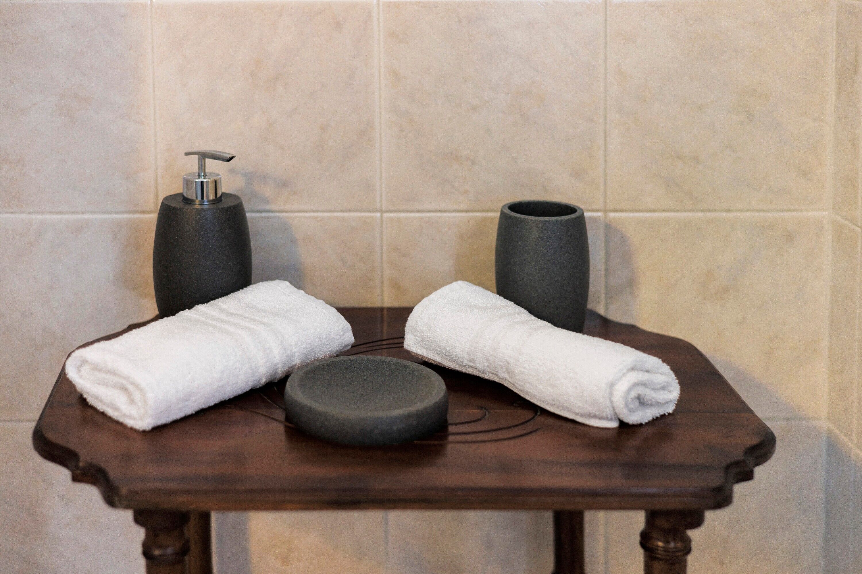 A bathroom with a wooden vanity, two white towels, a black soap dispenser, and a black vase.