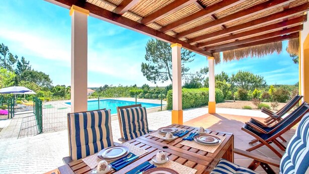 Un espace de restauration en plein air avec vue sur la piscine, des tables en bois, des chaises à rayures et une pergola au-dessus.