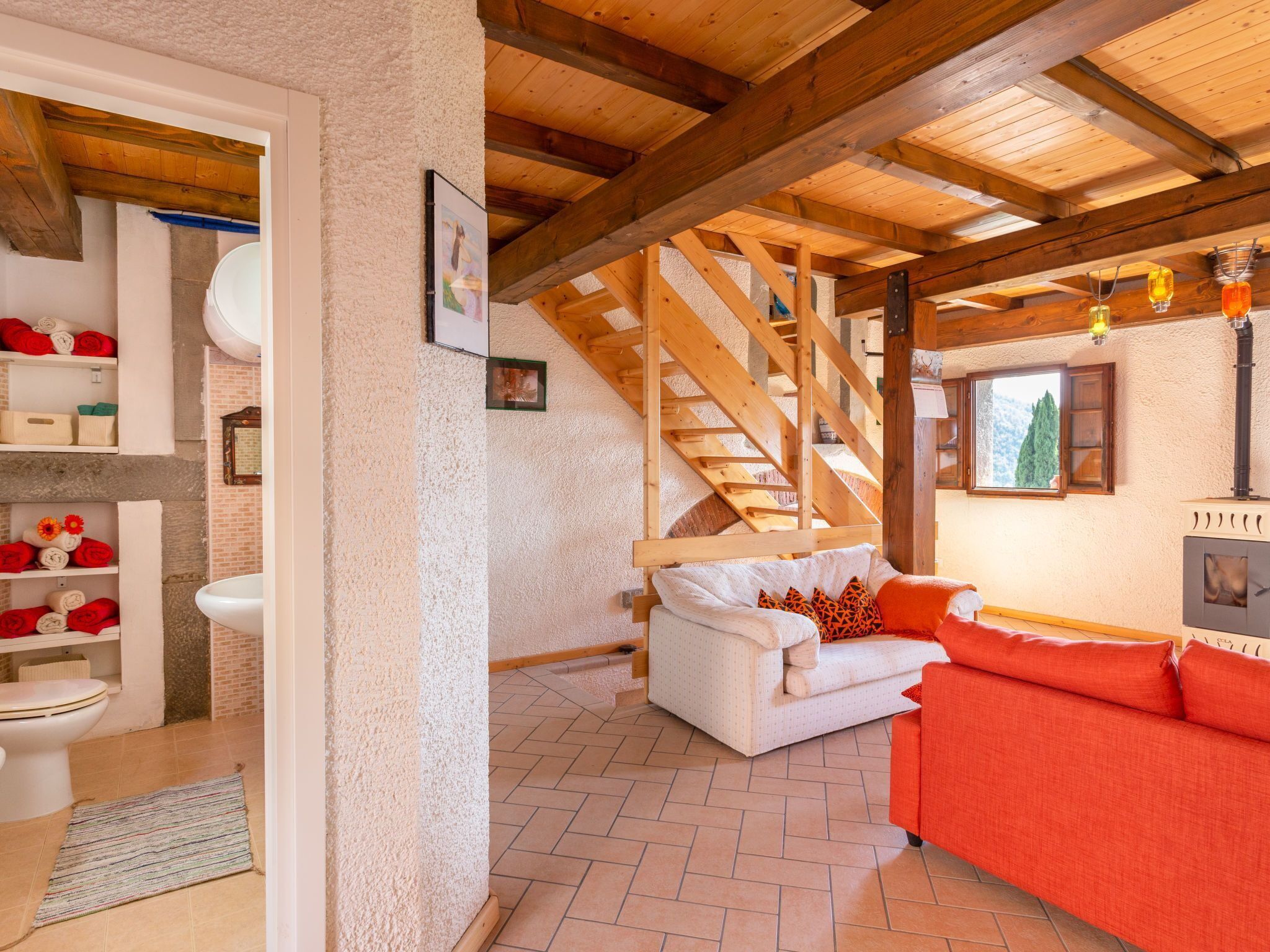 Un intérieur rustique avec un escalier en bois, un canapé blanc, un canapé rouge et une cheminée.