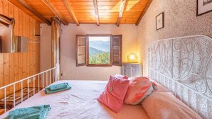Un dormitorio con techo de madera, cama con almohadas, mesita de noche con lámpara y ventana con vistas a la vegetación.