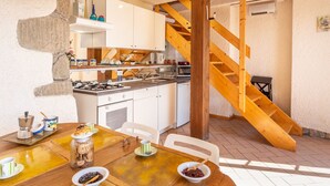 Una cocina con escalera de madera, armarios blancos y un comedor con una mesa dispuesta para dos.