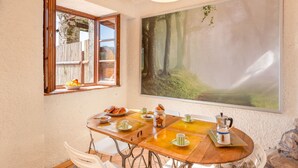 Un comedor con mesa de madera, sillas, un cuadro grande de un bosque y una ventana con vistas a una terraza de madera.