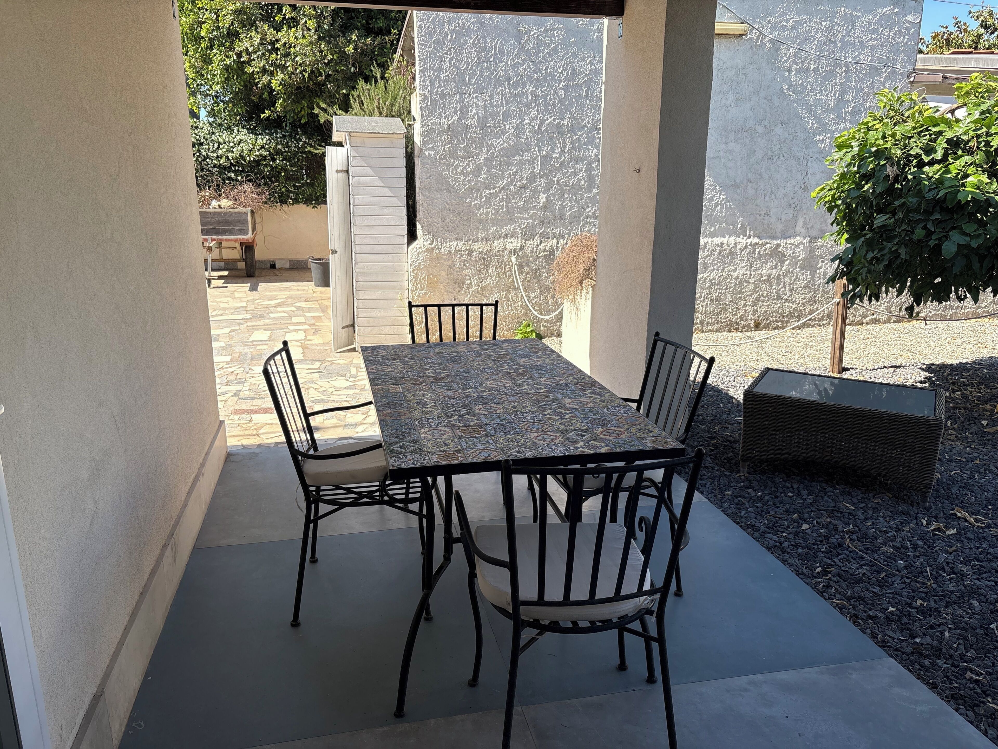 A covered patio with a table and chairs, a stone floor, and a view of a garden.