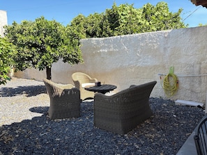 Gartenmöbel aus Rattan, ein Tisch und ein Gartenschlauch an einer Wand.