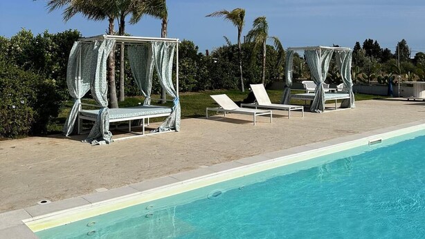 Zona de piscina con sillones de descanso y una zona de estar cubierta.