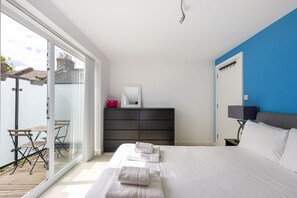 Ein Schlafzimmer mit einem Bett, einem Schminktisch, einem Spiegel, einem Nachttisch und Blick ins Freie.