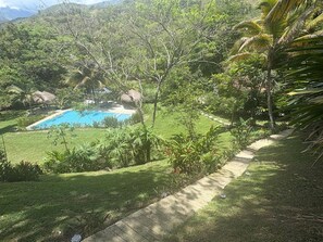 A lush garden with a swimming pool, surrounded by tropical vegetation and a stone pathway. - Finca La Verbena - The Sound of Nature (San Jerónimo)