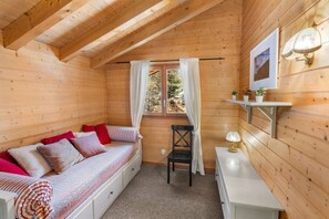 Une pièce chaleureuse, aménagée dans un chalet en bois, avec un lit, une chaise, une petite table et une fenêtre avec des rideaux.