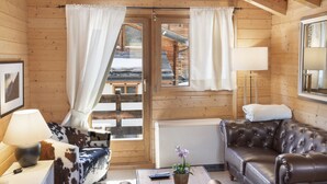 Interior de una cabaña de madera con sofá, lámpara, una mesa de centro y vista a una terraza de madera.