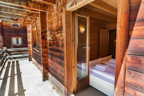 A wooden cabin with a glass door leading to a bedroom with a bed and a nightstand.