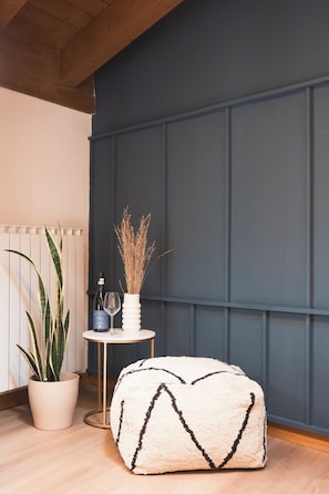 A room with a wooden floor, a white pouf with black stripes, a small round table with a bottle and glass, and a tall plant in a white pot. - Penthouse With View • 6 min walk to Bernina Express (Tirano)