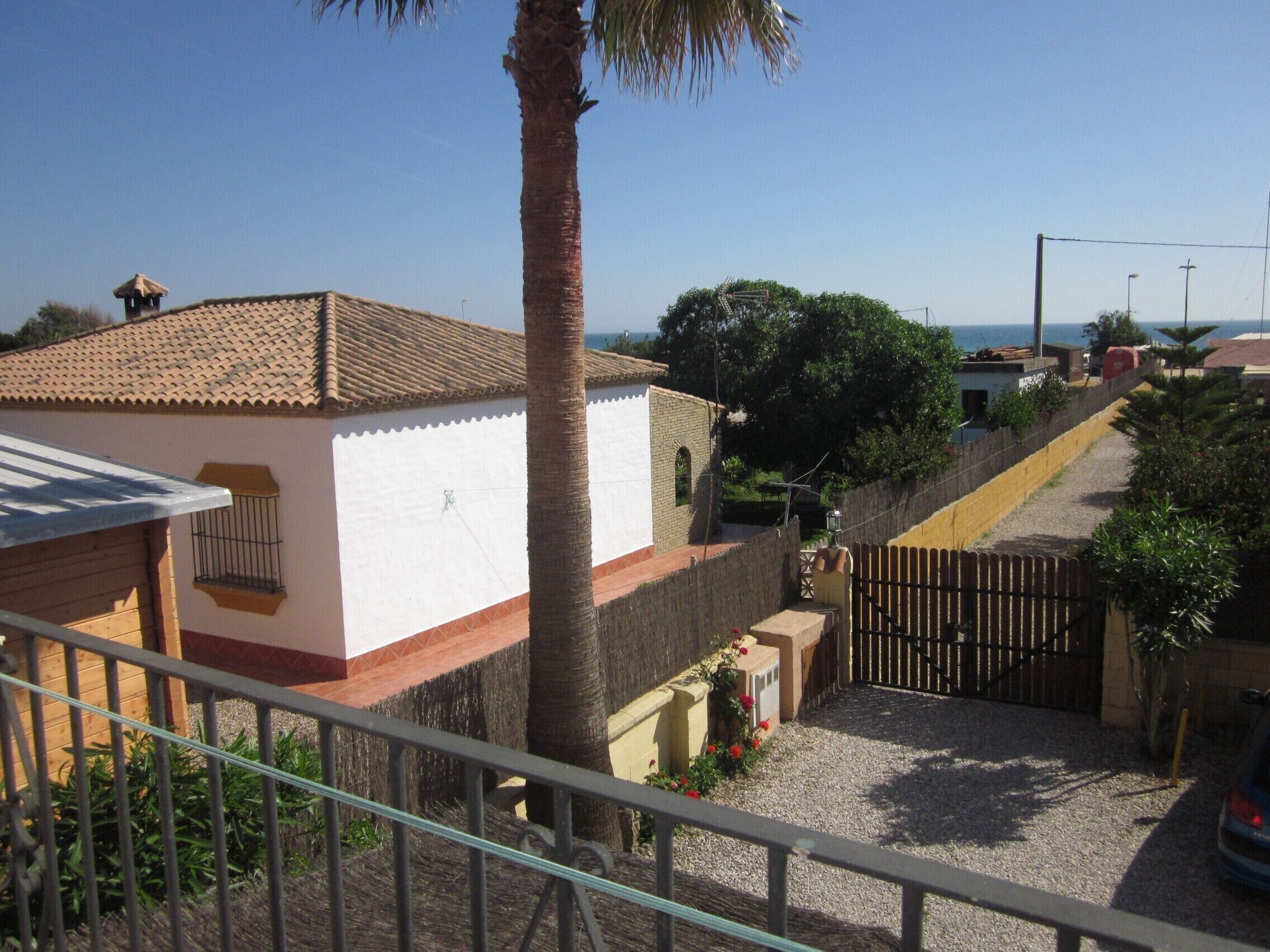 Un barrio residencial con una casa blanca, una palmera y un acceso con puerta de reja.