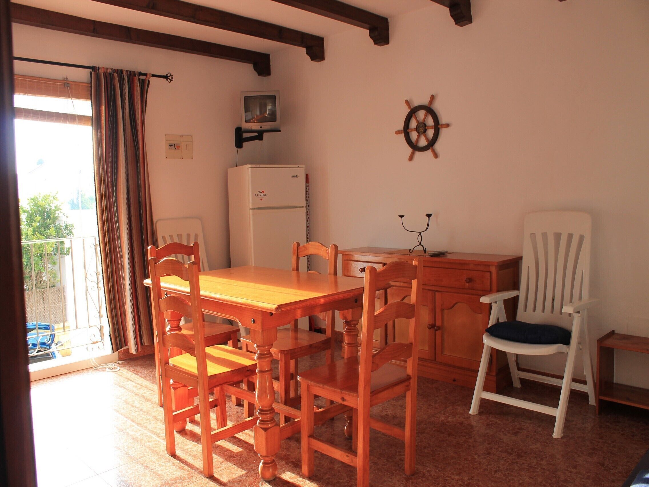 Un coin repas avec une table et des chaises en bois, un réfrigérateur blanc et un gouvernail de bateau fixé au mur.