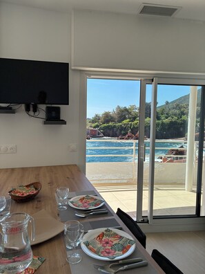 Ein Essbereich mit Tisch für zwei Personen, einem an der Wand montierten Fernseher und Blick auf den Ozean durch große Schiebeglastüren.