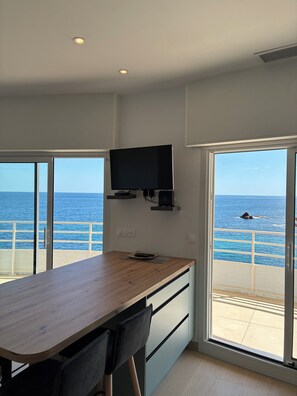 A modern room with a wooden table, chairs, a flat-screen TV mounted on the wall, and large windows offering a view of the sea. - Apartment on the sea Clim heated pool parking (Saint-Raphaël)